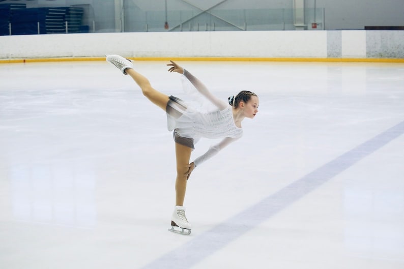 A new figure skating dress "Overture" for performances and competitions. The dress is made in the ombre technique and hand-painted with an airbrush from clear white to gray and obsidian black! Girl in the "Overture" dress on ice