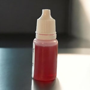 Peut inclure: Un petit flacon en plastique transparent avec un compte-gouttes blanc. Le flacon est rempli d'un liquide rouge vif.