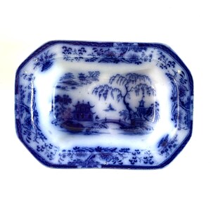 May include: An antique blue and white rectangular dish with a detailed landscape scene. The dish has a decorative border and a central image of a pagoda, bridge, and trees. The dish is likely made of porcelain.