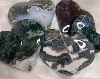 May include: A collection of five heart-shaped polished stones featuring various patterns and colors. The stones display shades of deep forest green, translucent white, grey, and dark brown, with intricate moss-like inclusions and smooth, glossy surfaces.