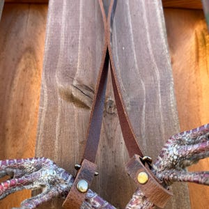 May include: Two brown leather straps with metal buckles attached to a pair of turkey feet.