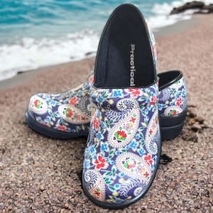 May include: A pair of clogs with a colorful paisley pattern in red, blue, green, and yellow. The clogs have a navy blue base and a black sole. The word "Practical" is printed on the inner sole.