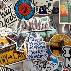 May include: A collection of various New York City themed stickers featuring iconic imagery including the Statue of Liberty, yellow taxis, the Brooklyn Bridge, a pigeon, and Hello Kitty. Text includes New York, Brooklyn, and It will Always be New York or Nowhere.