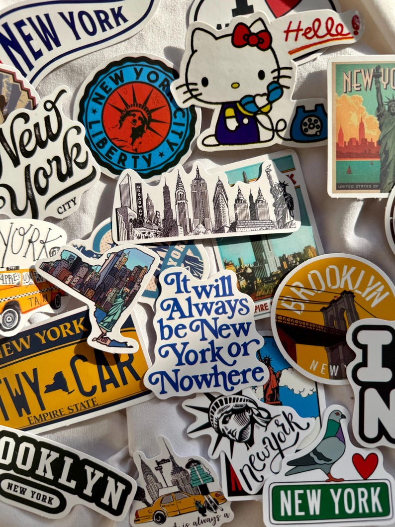 May include: A collection of various New York City themed stickers featuring iconic imagery including the Statue of Liberty, yellow taxis, the Brooklyn Bridge, a pigeon, and Hello Kitty. Text includes New York, Brooklyn, and It will Always be New York or Nowhere.
