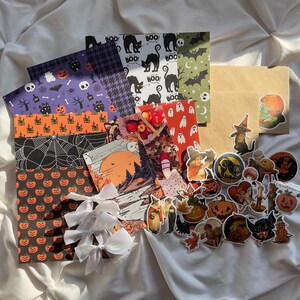 May include: A collection of Halloween themed wrapping paper, stickers, and decorative bows. The wrapping paper features various designs including pumpkins, ghosts, bats, and black cats. The stickers feature vintage-style illustrations of pumpkins, ghosts, and other Halloween imagery. The bows are white and made of satin.