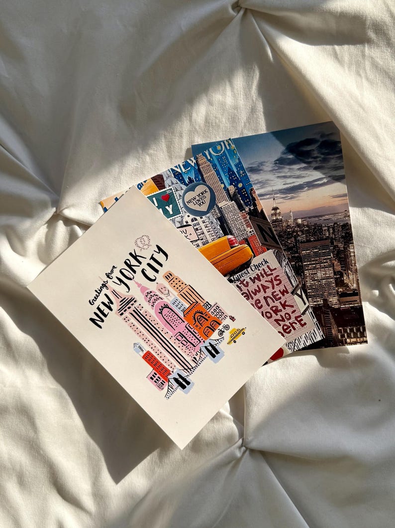May include: Three rectangular postcards featuring New York City themes. One postcard displays a stylized illustration of skyscrapers with the text Greetings from NEW YORK CITY. Another shows a yellow taxi and city skyline. The third is a night view.