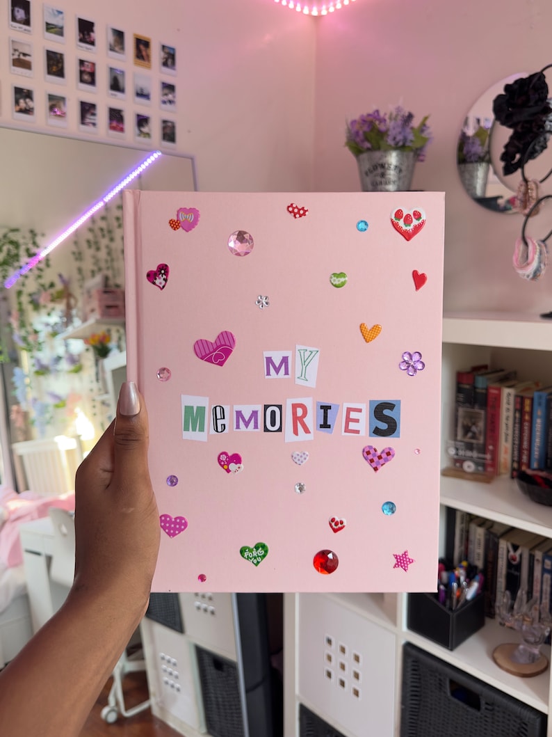 May include: Pink scrapbook with the words "MY MEMORIES" spelled out in colorful letters. The scrapbook is decorated with hearts, stars, and rhinestones.
