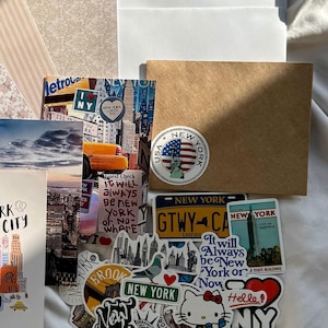 May include: A collection of New York City themed stickers and postcards featuring iconic imagery like the Statue of Liberty, yellow taxis, skyscrapers, and the Hello Kitty character. The items include various text designs such as New York, I Love NY, and It will always be New York or Nowhere.