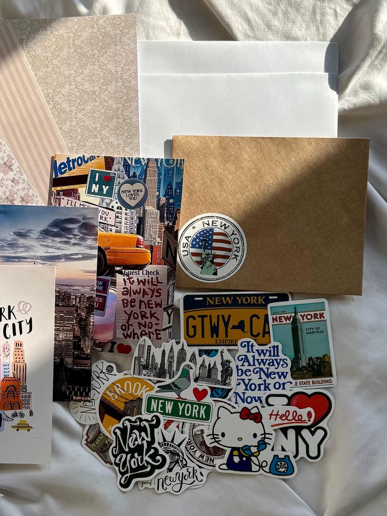 May include: A collection of New York City themed stickers and postcards featuring iconic imagery like the Statue of Liberty, yellow taxis, skyscrapers, and the Hello Kitty character. The items include various text designs such as New York, I Love NY, and It will always be New York or Nowhere.