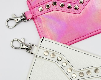 May include: Two small zippered pouches with silver studs and a silver clasp. The pouch on the top is pink with a holographic finish. The pouch on the bottom is white.