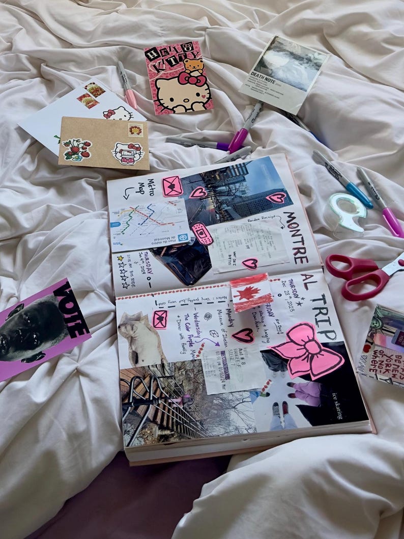 May include: An open journal with pink and white pages filled with stickers, photos, and handwritten notes. The journal is on a white bedspread with other stickers and pens scattered around it. The journal includes the text "MONTRE AL TRIP" and "THURSDAY Dec 28 2025".