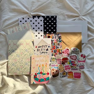 May include: A collection of birthday-themed stationery and stickers. Includes patterned paper, cards with "Happy Birthday" text, and various cake-themed stickers. The color palette features pastels and bright colors.