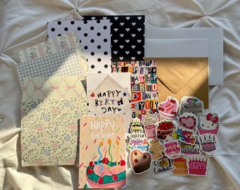 Könnte beinhalten: Eine Sammlung von Schreibwaren und Aufklebern zum Thema Geburtstag. Enthält gemustertes Papier, Karten mit dem Text "Happy Birthday" und verschiedene Aufkleber mit Kuchenmotiven. Die Farbpalette umfasst Pastelltöne und leuchtende Farben.