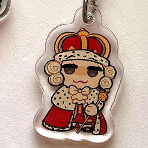 K&ouml;nnte beinhalten: Ein durchsichtiger Acryl-Schl&uuml;sselanh&auml;nger mit einer Comicfigur, die eine rot-goldene Krone, eine wei&szlig;-goldene Robe tr&auml;gt und ein goldenes Zepter h&auml;lt.
