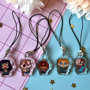 May include: Five colorful character phone charms with black cords. The charms are made of clear plastic with cartoon characters inside. The characters are a girl with black hair, a boy with brown hair, a boy with orange hair, a boy with blonde hair, and a boy with bandages on his head.