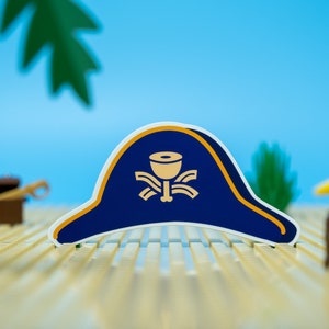 May include: A blue and gold pirate hat sticker with a skull and crossbones design. The sticker is on a light brown surface.