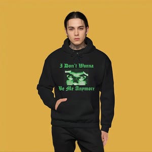 K&ouml;nnte beinhalten: Ein schwarzer Kapuzenpullover mit einem gr&uuml;nen Grafikdruck von Augen einer Person und dem Text "I Don't Wanna Be Me Anymore".