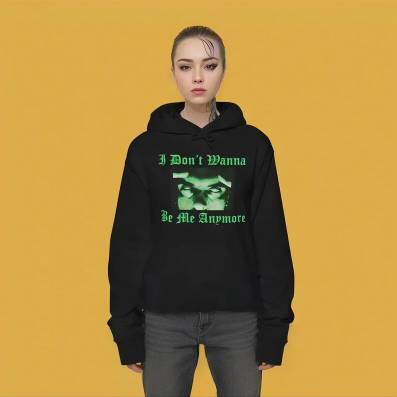 K&ouml;nnte beinhalten: Schwarzer, kurzer Hoodie mit einem gr&uuml;nen Grafikdruck eines Gesichts und dem Text "I Don't Wanna Be Me Anymore".
