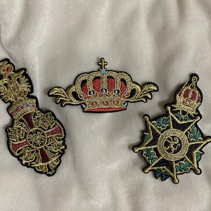 May include: Three embroidered iron-on patches. One features a gold crown with red jewels, another a gold cross with a red center, and the last a gold star with green foliage.