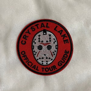 May include: Red and black embroidered patch with a white hockey mask and the text "Crystal Lake Official Tour Guide".