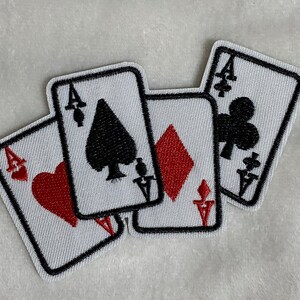May include: Embroidered patches featuring the aces of hearts, spades, diamonds, and clubs. Each card has a white background with black borders and the suit symbols in red or black. A fun accessory for clothing or bags.