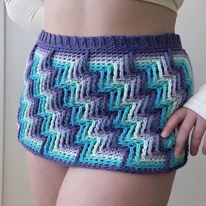 May include: A crocheted skirt with a geometric pattern in shades of purple, blue, and green.