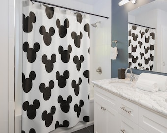 Puede incluir: Una cortina de ducha blanca con un patrón repetitivo de siluetas negras de la cabeza de Mickey Mouse. La cortina está suspendida de una barra negra con anillas metálicas en un baño, reflejándose el diseño en el espejo del lavabo.