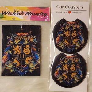 May include: Two round black car coasters with a colorful Hogwarts crest design. The coasters are handmade with love. The text "Wick'ed Novelty" is on a pink and white label.