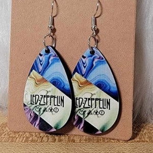 May include: A pair of teardrop-shaped wooden earrings with a blue, purple, and gold marbled design. The earrings feature the text "LED ZEPPELIN" in black lettering.
