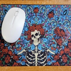 May include: A mouse pad with a colorful design featuring a skeleton with a skull and roses. The background is a blue and green floral pattern.