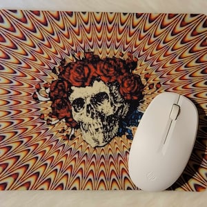 May include: A psychedelic mouse pad with a skull and flower design. The mouse pad is orange, yellow, and purple with a swirling pattern. A white wireless mouse is on top of the mouse pad.