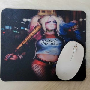 May include: A black and white mousepad with a colorful illustration of Harley Quinn. She is wearing a red and black costume, holding a baseball bat, and has a bubble in her mouth. The text "Daddy's Lil Monster" is printed on her shirt.