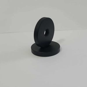 May include: Two black, circular objects with a hole in the center. One is lying flat, and the other is standing upright on top of it. The objects appear to be made of a solid material.