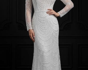 May include: A white, off-the-shoulder formal gown with long sleeves. The dress is embellished with intricate beadwork in a flowing, linear pattern. The gown has a fitted bodice and a floor-length skirt, suitable for a wedding or special occasion.