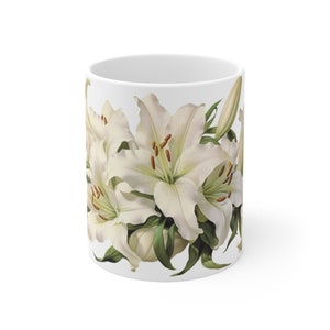 May include: White ceramic mug with a floral design featuring white lilies with green leaves.