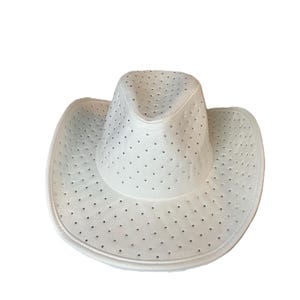 May include: White cowboy hat with a perforated design. The hat features a wide brim and a rounded crown. Small, evenly spaced holes cover the entire hat, adding a decorative element. The hat is made of a smooth material.
