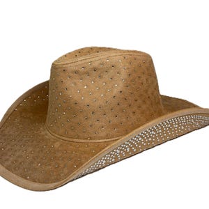 May include: A tan cowboy hat with a wide brim and a rounded crown. The hat is adorned with small, sparkling rhinestones scattered across the surface and along the brim. The hat is made of a suede-like material.