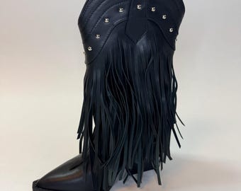 May include: Black leather cowboy boot with a pointed toe and fringe detail. The boot features silver-tone studs along the top and a decorative stitched pattern. The boot is set against a white background.