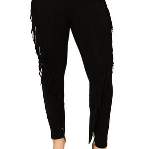 May include: Black leggings with fringe detailing along the outer seams. The leggings are made of a stretchy material and are designed to be form-fitting. The fringe adds a unique, stylish element to the garment. The model is wearing black heels.