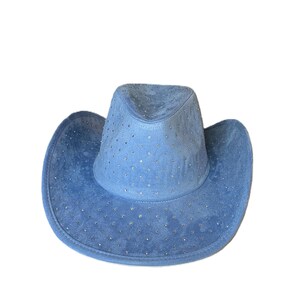 May include: A light blue cowboy hat with a suede-like texture. The hat is adorned with small, sparkling embellishments across the crown and brim. The hat has a classic cowboy hat shape with a rounded crown and a wide, curved brim.