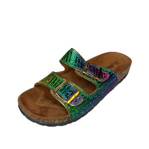 May include: A pair of iridescent rainbow-colored sandals with two adjustable straps and gold-colored buckles. The footbed is a light brown cork material. The straps are covered in small, sparkling rhinestones. The sandals are designed for casual wear.