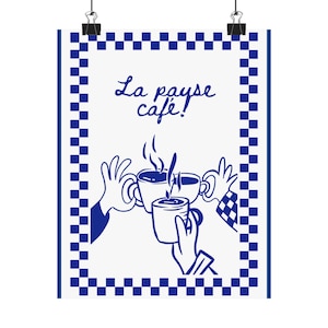 May include: A white poster with a blue checkered border and the words "La pause café!" in blue script. The image depicts three hands holding coffee cups, with steam rising from the cups. The poster is held by two black binder clips.