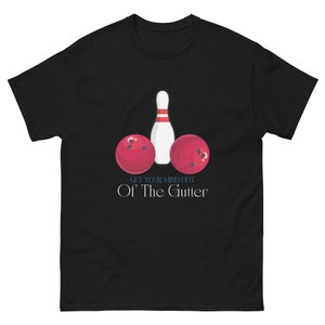 Puede incluir: Camiseta negra con un diseño de bolos y dos bolas rojas. El texto "GET YOUR MIND OUT Of The Gutter" está impreso debajo. La camiseta está hecha de un material suave y cómodo.