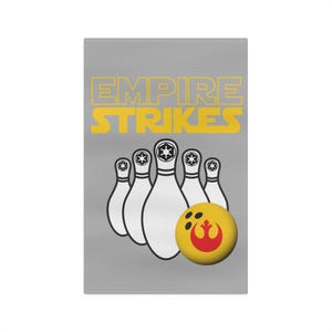 May include: A gray rectangular graphic featuring the text "EMPIRE STRIKES" in yellow. Below the text are white bowling pins with black details and a yellow bowling ball with a red graphic.