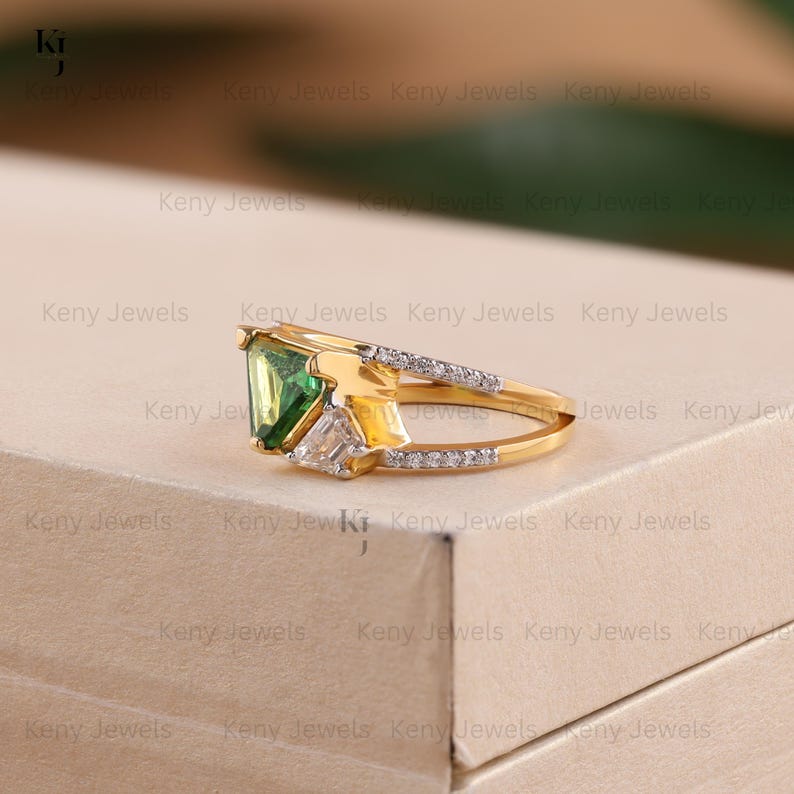 A double-band yellow gold ring holds a large, triangular green stone in a three-prong setting. A small cluster of sparkling white diamonds is set on the lower band right next to the central green gem.