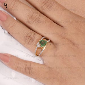 Close-up of a modern split-shank gold ring featuring a vibrant, triangle trillion-cut green tourmaline gemstone accented by a smaller asymmetric baguette diamond band.