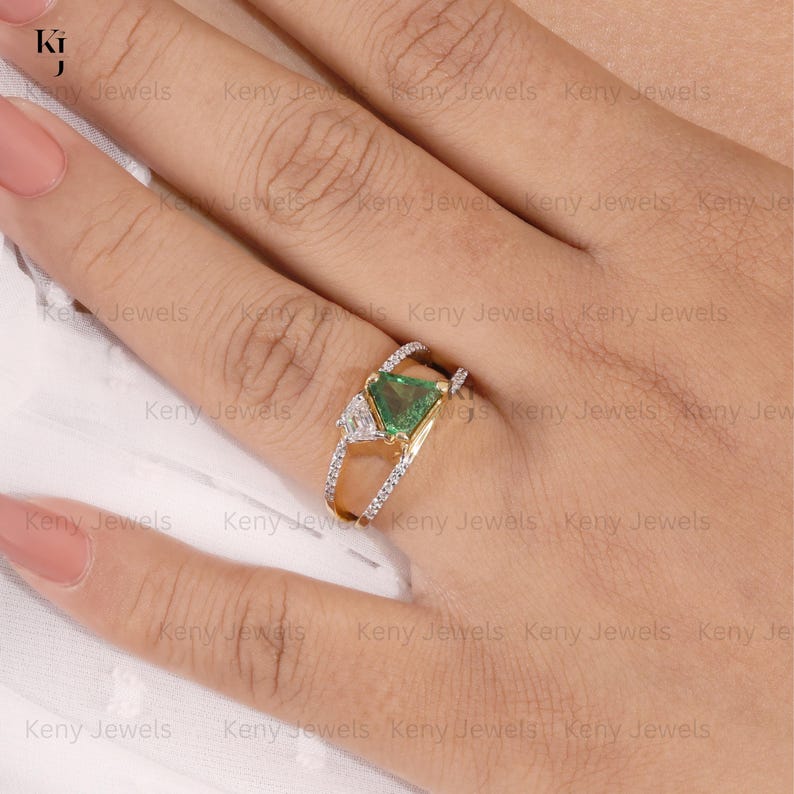 Close-up of a modern split-shank gold ring featuring a vibrant, triangle trillion-cut green tourmaline gemstone accented by a smaller asymmetric baguette diamond band.