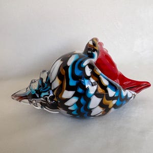 May include: A colourful glass seashell sculpture with a black, white, blue, gold, and red swirl pattern.