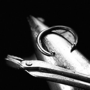 Puede incluir: Primer plano de un par de alicates de metal con un objeto en forma de anillo descansando encima. Los alicates están hechos de metal y tienen un acabado negro. El anillo también está hecho de metal y tiene un acabado plateado.