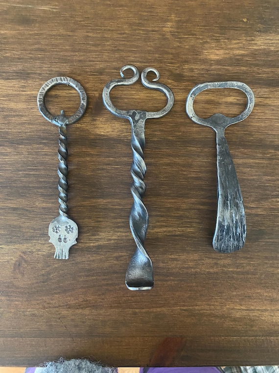A blacksmith literally hammered this bottle opener into existence — the kind of raw, functional iron craft that looks like it belongs in a medieval tavern.